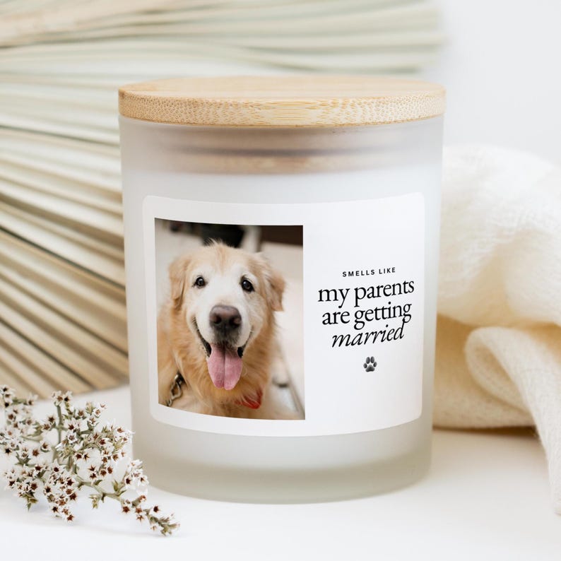 May include: A frosted glass candle with a wooden lid. The label features a photo of a golden retriever and the text "Smells Like my parents are getting married" with a paw print.