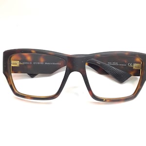 May include: Square-framed eyeglasses with a tortoise shell pattern. The glasses have a dark brown top frame and a lighter brown frame around the lenses. The text "JL...M814-10 57016-130 Made in Mauritius" is visible on the left arm.