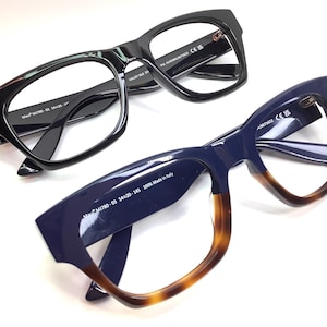 May include: Two pairs of spectacles. One pair is black with a rectangular frame. The other pair is navy blue with a tortoiseshell gradient on the lower frame. Both have clear lenses and black temples.