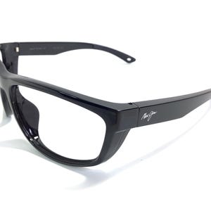 May include: Black eyeglasses with a thick, rectangular frame. The temples are wide and feature the brand name "Maui Jim" in white script. The lenses are clear, and the overall design is modern and sleek.