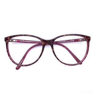 May include: A pair of eyeglasses with a brown tortoiseshell pattern on the frames and a magenta interior. The lenses are clear, and the arms are a matching magenta color. The glasses have a classic, oval shape.