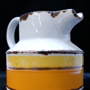 May include: A ceramic pitcher with a white top and handle, featuring a yellow and orange band around the middle. The rim and the bands are outlined with a dark brown color. The pitcher has a spout for pouring.