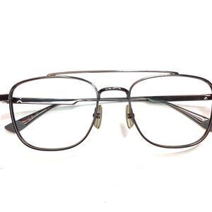 May include: Silver-toned aviator eyeglasses with a double bridge and clear lenses. The frames have a rectangular shape with rounded edges. The nose pads are a light beige color. The glasses are set against a white background.