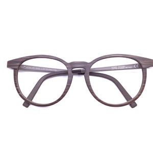 May include: Brown eyeglasses with a horizontal wood grain pattern on the round frames and temples. The inner side of the left temple features printed text including M1005-23C 53X18 L.145, and the right temple displays text including 510-50 0071622 CE.
