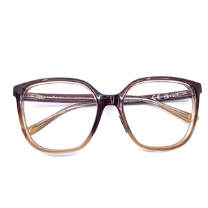 May include: Brown and tan gradient eyeglasses with a square frame. The glasses have clear lenses and a subtle design on the temples. The frame transitions from a dark brown at the top to a lighter tan at the bottom.