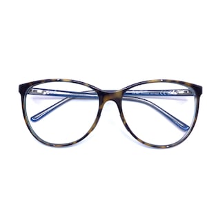 May include: Oval-shaped eyeglasses with a tortoiseshell pattern on the frames. The temples are a dark blue color. The lenses are clear. The glasses are set against a white background.