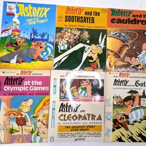 以下が含まれることがあります： アステリックスのコミック本6冊セット。タイトルは「Asterix and the Big Fight」、「Asterix and the Soothsayer」、「Asterix and the Cauldron」、「Asterix at the Olympic Games」、「Asterix and Cleopatra」、「Asterix and the Goths」で、カラフルなイラストが描かれています。