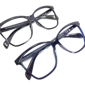 May include: Two pairs of black cat-eye glasses with clear lenses. The top pair has black frames and the bottom pair has blue frames.