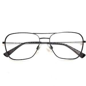 May include: Black aviator-style eyeglasses with a double bridge and clear lenses. The frames are a thin, dark metal. The temples have a textured design. The glasses are set against a white background.