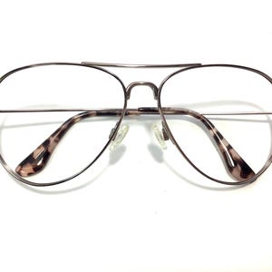 May include: Aviator-style eyeglasses with a silver metal frame and clear lenses. The temples feature a brown and tan tortoiseshell pattern. The glasses have a double bridge and nose pads.