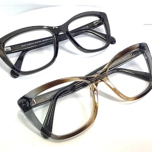 May include: Two pairs of eyeglasses with black frames. The top pair has a dark gray frame and the bottom pair has a brown frame.