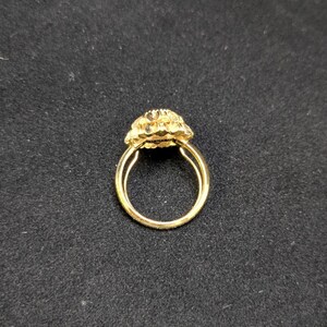 May include: A gold ring with a floral design. The ring features a double band and a cluster of small, textured petals forming the centerpiece. The ring is set against a dark background, highlighting its bright, shiny appearance.