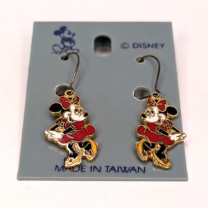 May include: A pair of Minnie Mouse dangle earrings. The earrings feature a gold-colored outline with black, red, white, and yellow enamel details. The earrings are attached to a gray card that reads "&copy; DISNEY" and "MADE IN TAIWAN."
