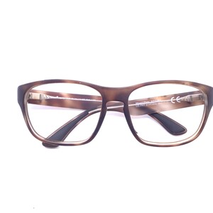 May include: Tortoiseshell-patterned eyeglasses with a brown frame and clear lenses. The inner temple arm features the text Maui Jim 570-56 US PAT 6145984 6877847 CE. The frame has a rounded rectangular shape with black accents on the inner temple tips.