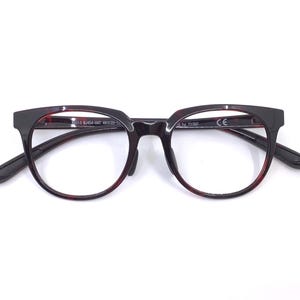 May include: A pair of eyeglasses with a dark brown and black frame. The glasses have a round lens shape with a red-brown interior rim. The arms are black and the frame has a rectangular top. The glasses are set against a white background.