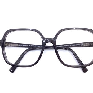 May include: Dark gray, square-framed eyeglasses with clear lenses. The glasses have a thick frame and a keyhole bridge. The arms of the glasses are thin and curve down to the ear. The text "MAUI MJ880-11 55 18-145 100% Made in" is printed on the left arm.