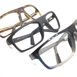 May include: Three pairs of eyeglasses with clear lenses are displayed. One pair has a brown tortoiseshell pattern, another is matte black, and the third transitions from gray to blue. The frames are modern and rectangular.
