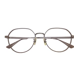 May include: Round-framed eyeglasses with a thin, dark metal frame. The lenses are clear, and the nose bridge and arms are a matching dark color. The glasses have a minimalist design, suitable for everyday wear.