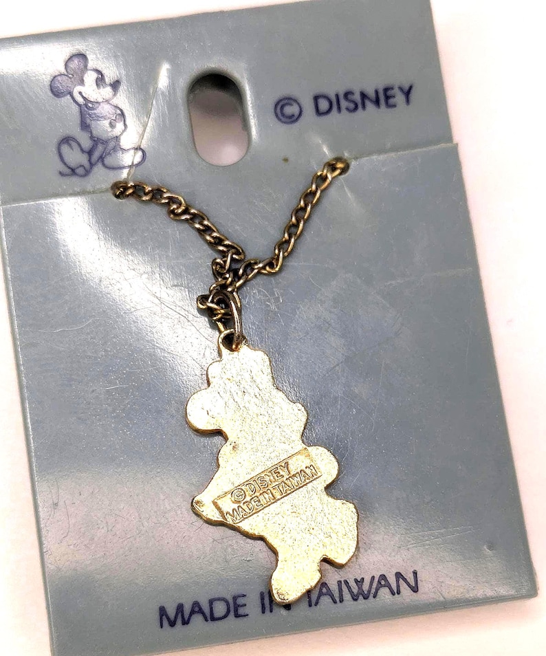 May include: Vintage Mickey Mouse pendant on a chain, attached to a blue card. The pendant is gold-colored and shaped like Mickey Mouse. The card has the Disney logo and the text "MADE IN TAIWAN".