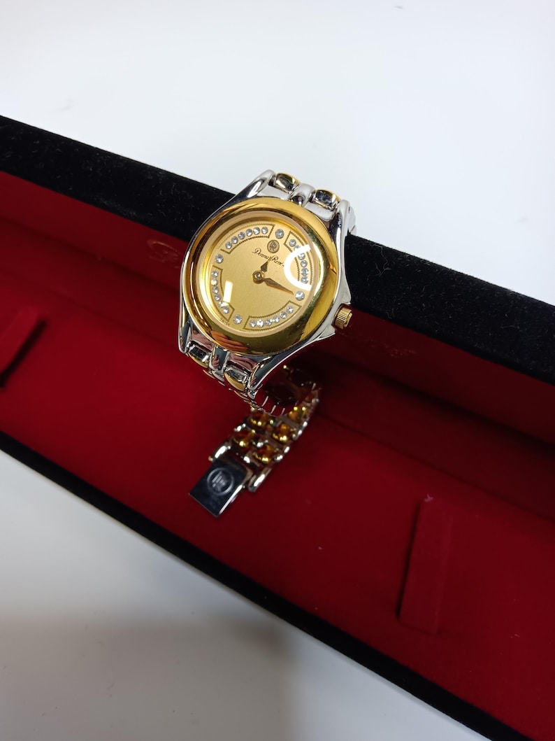 May include: A gold and silver wristwatch with a gold face and diamond accents. The watch is in a black box with a red interior. The watch band is silver and gold.