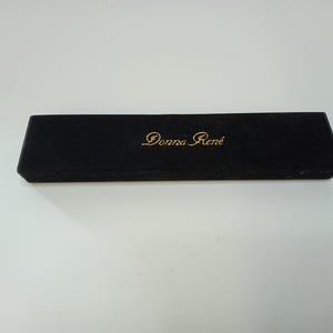 May include: A black rectangular box with the gold text "Donna Ren&eacute;" on the top. The box has a velvet-like texture and is set against a white background. The box is closed.