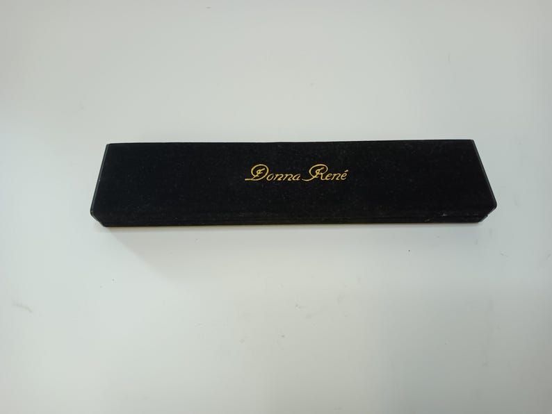 May include: A black rectangular box with the gold text "Donna Ren&eacute;" on the top. The box has a velvet-like texture and is set against a white background. The box is closed.