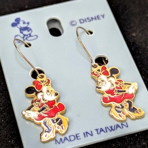 May include: A pair of gold-toned Minnie Mouse dangle earrings. Each earring features a red dress, black ears, and a white face. The earrings are on a light blue card with the Disney logo and "MADE IN TAIWAN".