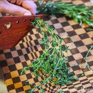 May include: A wooden tool with holes for stripping herbs, shown being used to strip thyme on a chequered chopping board.