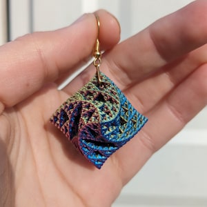 May include: A pair of earrings with a geometric, iridescent, blue, green, and purple cube-shaped pendant.