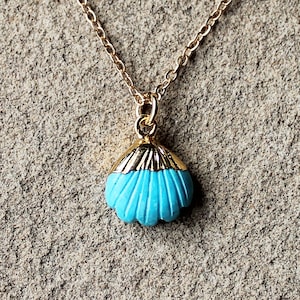 May include: A gold chain necklace with a turquoise seashell pendant. The seashell is detailed with gold accents and has a textured surface.