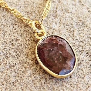 Puede incluir: Un collar de cadena de oro con un colgante ovalado marrón con una piedra preciosa. El colgante tiene un engaste de oro.