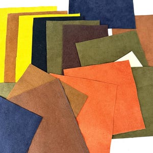 May include: A collection of colorful suede leather squares in various shades, including yellow, orange, brown, green, and blue. The pieces are arranged in a layered, overlapping pattern, showcasing the different textures and hues of the material.