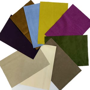 May include: A collection of rectangular fabric swatches in various colors, including purple, brown, blue, yellow, green, and beige. The swatches are arranged in a fan shape against a white background, showcasing the different textures and hues.