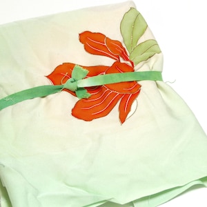 May include: A green fabric square with a large orange flower design tied with a green ribbon.