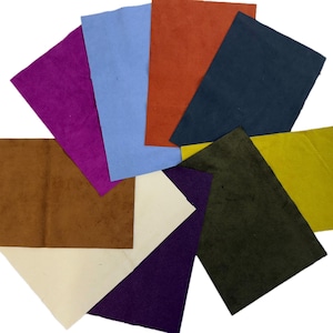 Puede incluir: Una colección de hojas de papel texturizadas y coloridas en varios tonos, incluyendo morado, azul, naranja y verde. Las hojas están dispuestas en forma de abanico, mostrando sus diversos tonos y texturas. El papel parece hecho a mano.