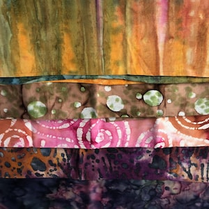 May include: A stack of colorful, hand-dyed fabric pieces. The textiles display a variety of patterns and colors, including orange, brown, pink, purple, and blue. Some fabrics feature spiral and spotted designs, while others have a more abstract appearance.