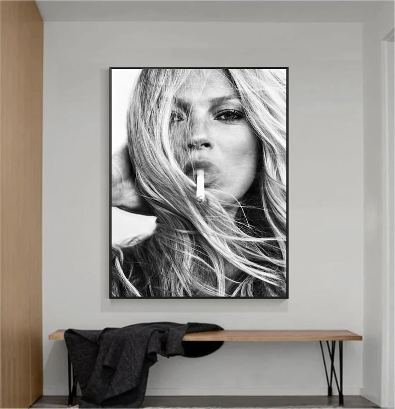 May include: Black and white photograph of a woman with long blonde hair, looking directly at the camera. She is holding a cigarette in her mouth.