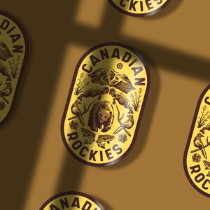 May include: A yellow and brown oval sticker with the text "Canadian Rockies" in a brown circle. The sticker features a brown bear, a mountain range, and other wildlife.