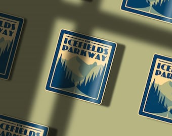 May include: Blue and white sticker with the text "The Icefields Parkway" in a vintage style font. The sticker features a mountain landscape with trees and a road.