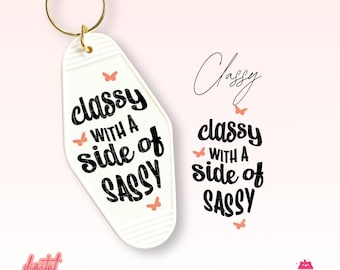 May include: A white motel-style keychain with the phrase "classy with a side of sassy" in black script. Small peach butterflies accent the design. A gold key ring is attached. A matching graphic is also displayed.