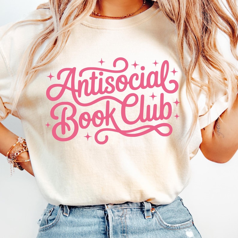 K&ouml;nnte beinhalten: Cremefarbenes T-Shirt mit dem pinkfarbenen Schriftzug "Antisocial Book Club" in verschn&ouml;rkelter Schrift. Der Text ist von kleinen Sternen umgeben. Das Shirt besteht aus weichem Material und hat kurze &Auml;rmel.