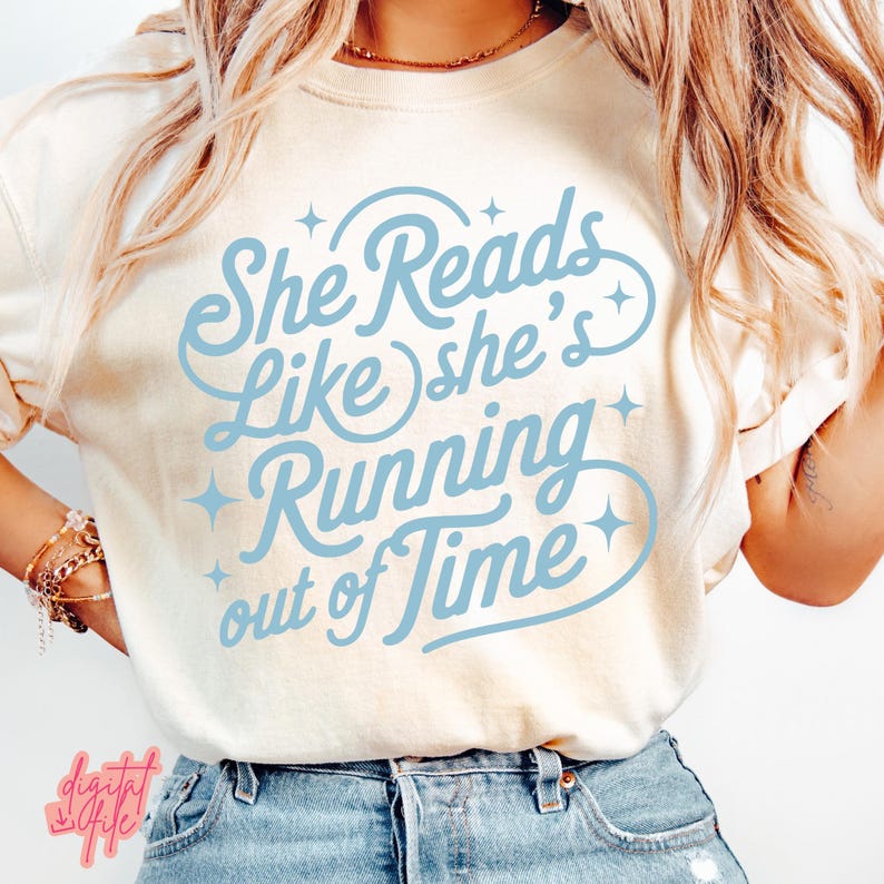 May include: Cream-colored t-shirt with the text "She Reads Like she's Running out of Time" in light blue script. The design includes star accents. The shirt is worn with blue jeans.