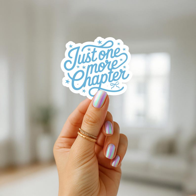 K&ouml;nnte beinhalten: Ein hellblauer Aufkleber mit dem Text "Just one more Chapter" in einer verspielten Schriftart. Der Aufkleber hat eine wolkenartige Form mit kleinen Sternen und einer Schleife. Der Aufkleber wird von einer Hand mit schillernden N&auml;geln und goldenen Ringen gehalten.