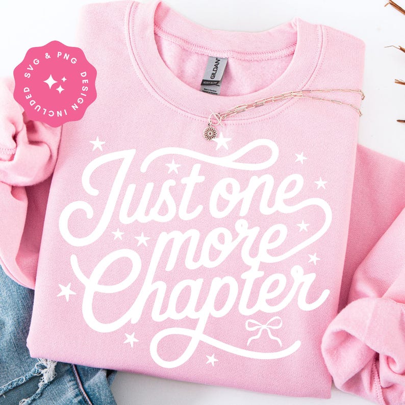 K&ouml;nnte beinhalten: Ein hellrosa Sweatshirt mit dem wei&szlig;en Schriftzug "Just one more chapter". Das Design beinhaltet Sterne und eine Schleife. Eine goldene Halskette mit einem Blumenanh&auml;nger liegt auf dem Sweatshirt. Eine rosa SVG & PNG Design-Grafik befindet sich in der oberen linken Ecke.