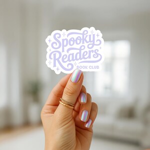 May include: A die-cut sticker featuring the text Spooky Readers BOOK CLUB in a light purple cursive font, accented with small four-pointed star icons. The sticker has a white border and a matte finish, displaying a whimsical design for book lovers.