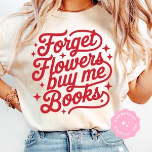 Puede incluir: Camiseta color crema con el texto rojo "Forget Flowers buy me Books" en escritura cursiva, con detalles de estrellas. La camiseta se lleva con vaqueros azules.