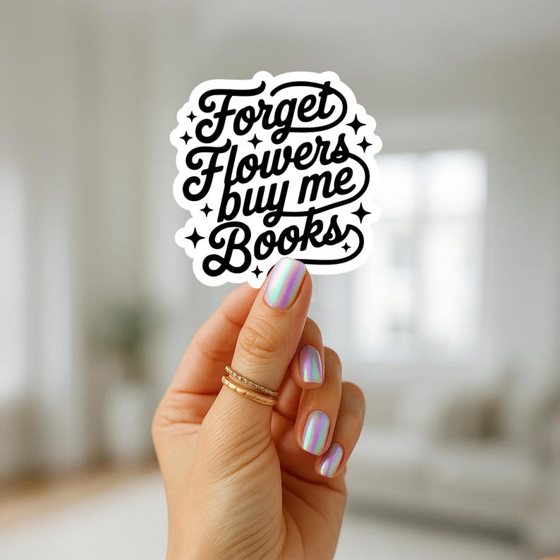 Puede incluir: Una pegatina blanca con el texto "Forget Flowers buy me Books" en una fuente negra y estilizada. La pegatina est&aacute; sujeta por una mano con esmalte de u&ntilde;as iridiscente y anillos dorados.