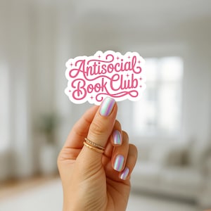 K&ouml;nnte beinhalten: Ein wei&szlig;er Aufkleber mit dem Text "Antisocial Book Club" in rosa Schrift. Der Aufkleber wird von einer Hand mit schillerndem Nagellack und goldenen Ringen gehalten. Das Design weist dekorative Verzierungen und Sterne auf.