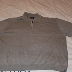 May include: A gray quarter-zip sweater with a mock neck collar. The sweater has long sleeves and a ribbed hem. The zipper is partially open. The sweater is lying flat on a white surface.