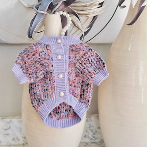 May include: A purple and multi-colored knitted sweater with pearl buttons. The sweater has a short sleeve and a button-up front.